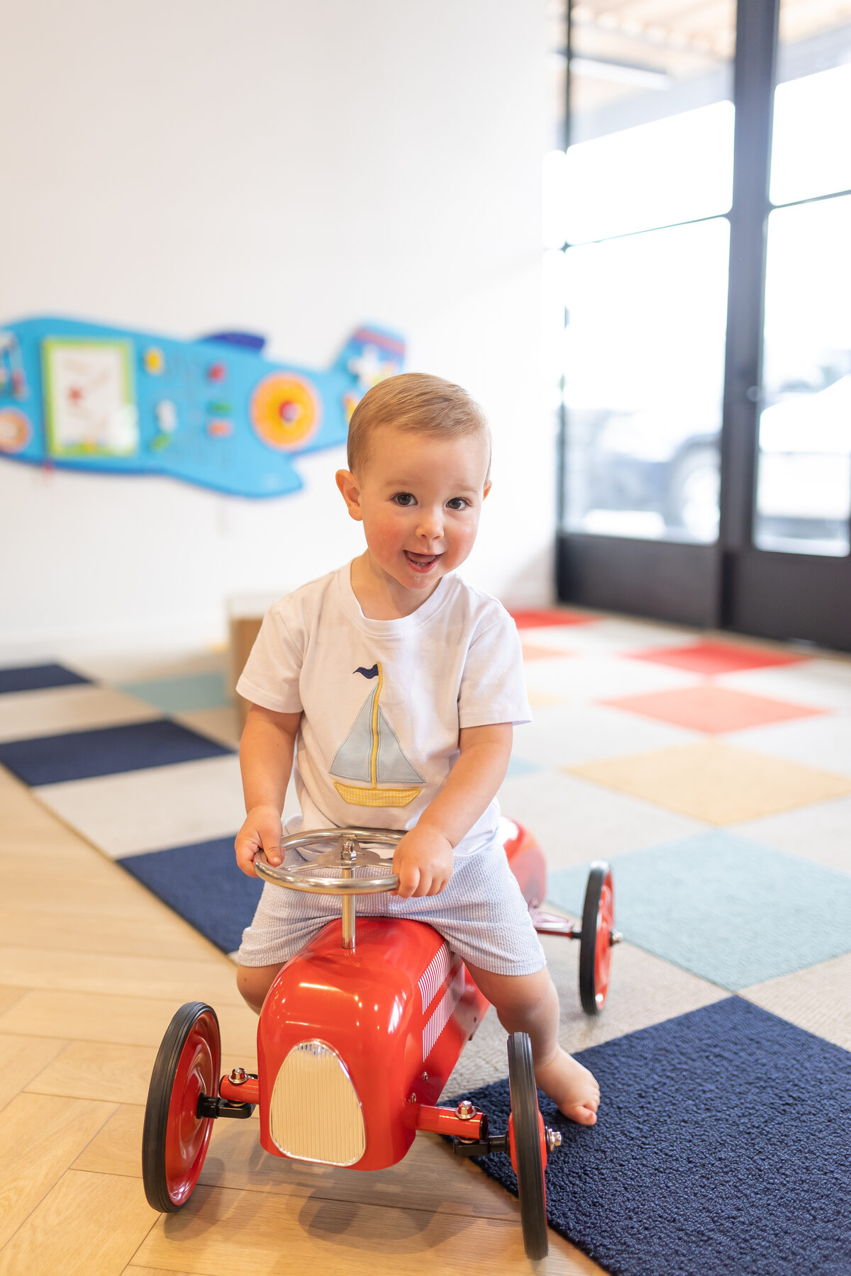 Toddler smiling on a red ride-on car at The Little Play Avenue